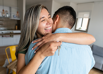 Two people hugging happily. One holds a house key.