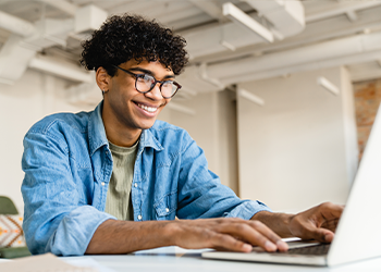 A young person smiles at a laptop screen